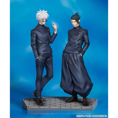 Figures of Satoru Gojo and Suguru Geto from Jujutsu Kaisen. Gojo is on the left with white spiky hair and blue-tinted glasses, wearing a dark outfit, while Geto is on the right with his hair tied up in a bun, dressed in a similar dark high-necked outfit, both standing against a blue sky background